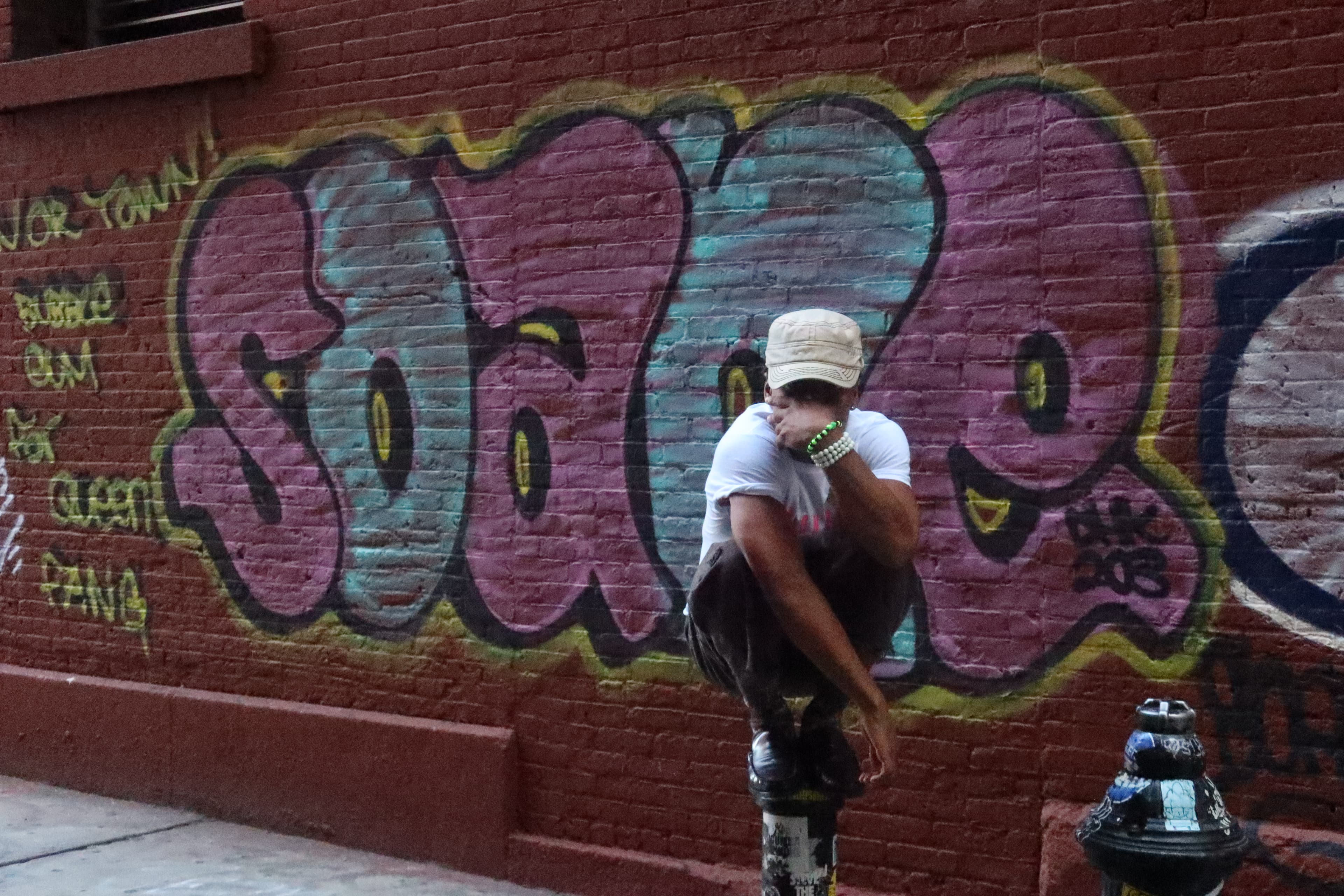 FaurY perched on a fire hydrant against a graffiti wall in Soho