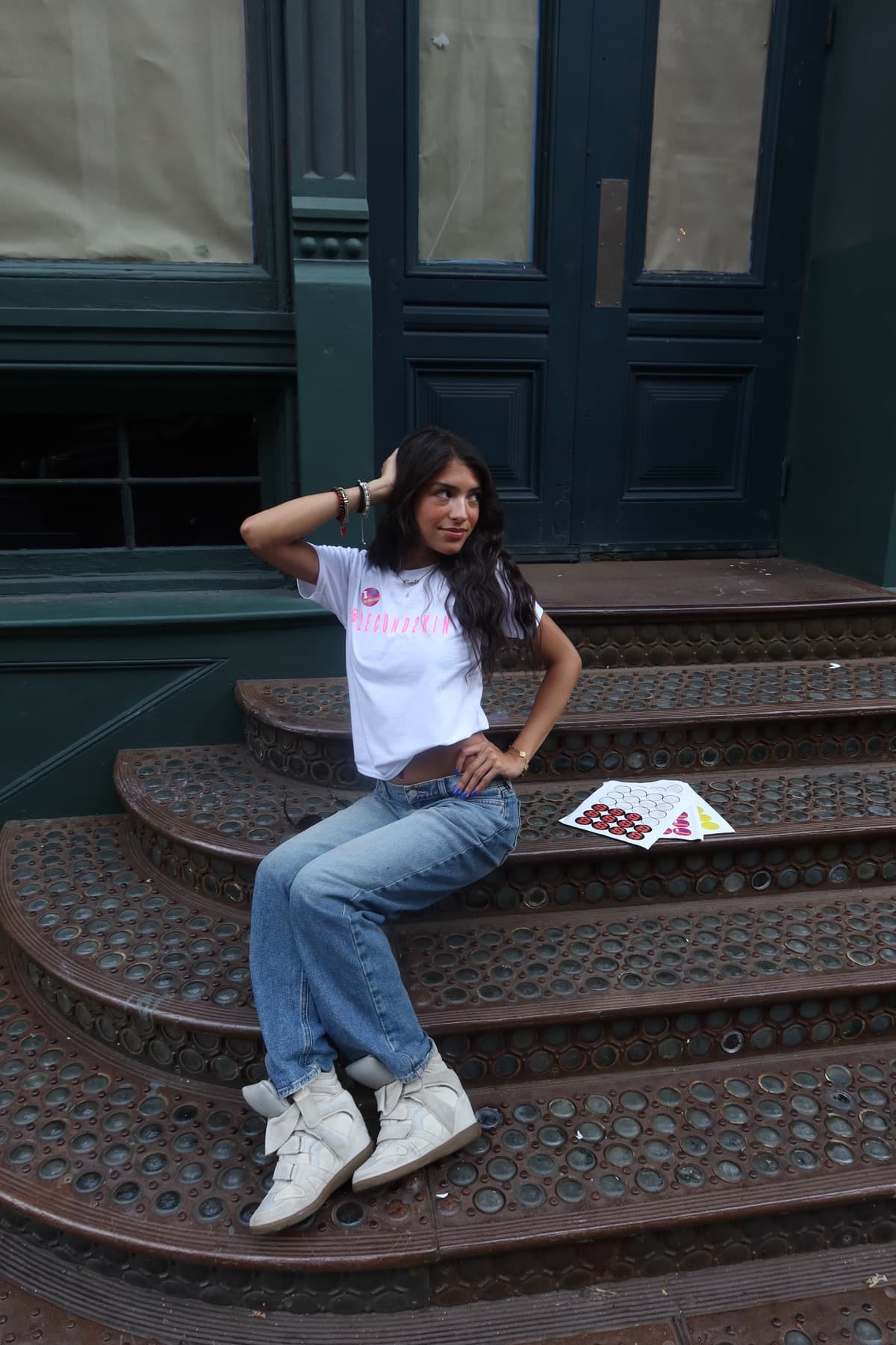 Model seated on brownstone steps, hand in hair, smiling